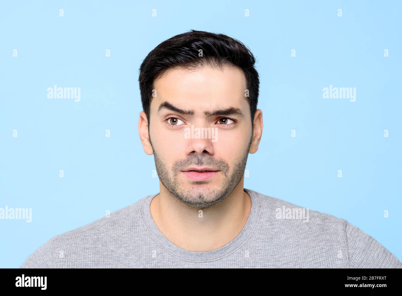 Nachdenklich neugieriger junger Mann Gesicht mit Augenbraue isoliert auf hellblauem Hintergeschirn Stockfoto
