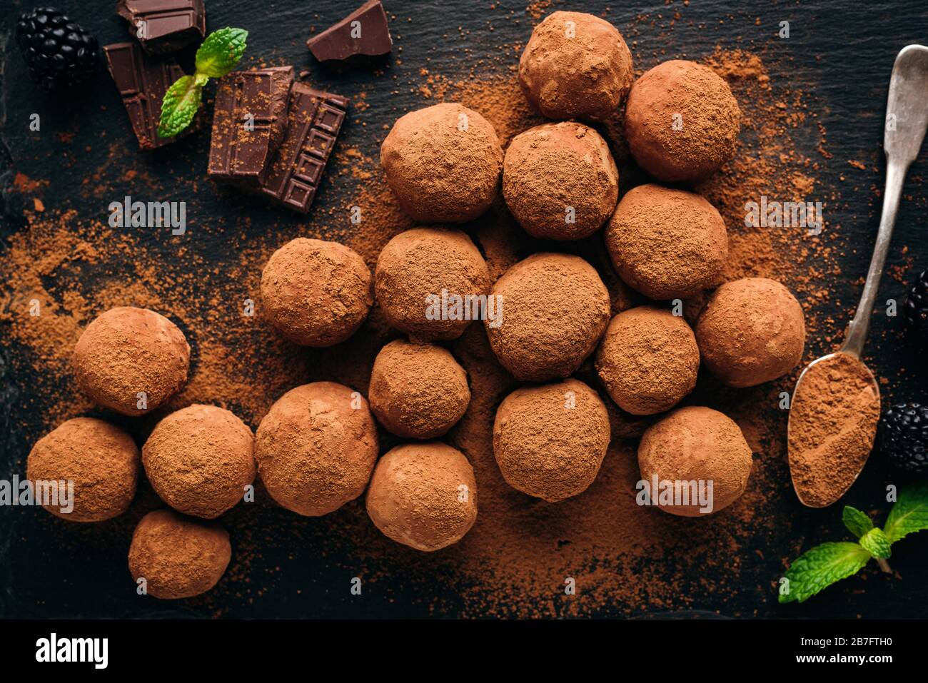 Schokoladentrüffeln auf schwarzem Grund in gemahlenem Rohkakaopulver gerollt. Hausgemachte schmackhafte Schokoladenbonbons Stockfoto