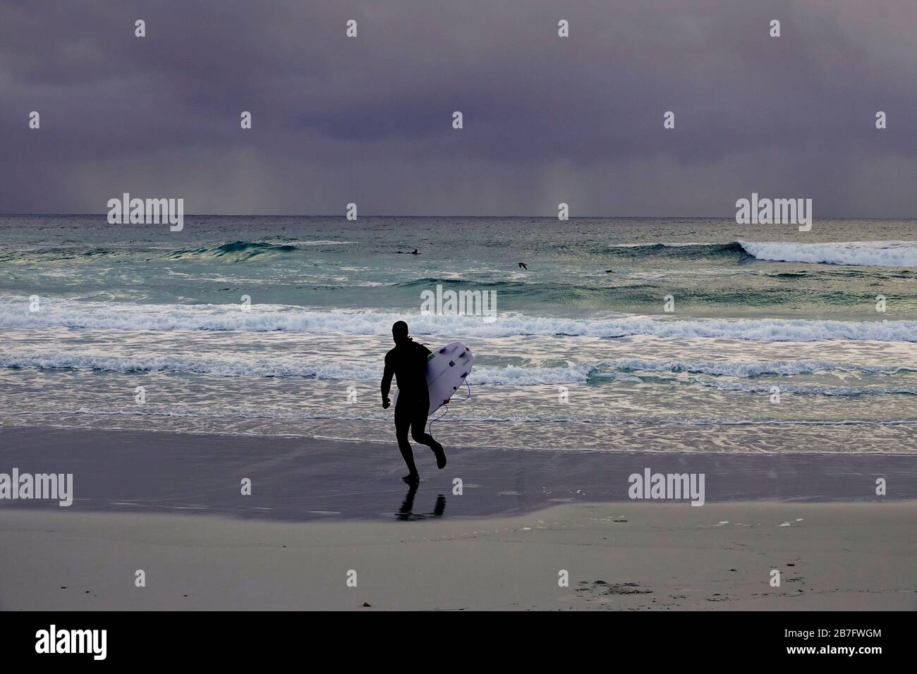 Monterey, Kalifornien, USA. März 2020. Ein einsamer Surfer geht auf den Ozean hinaus, während sich Sturmwolken über dem Pazifik vor Monterey, Kalifornien, sammeln, um noch mehr zu dämpfen, die Stimmung eines depressiven Staates, der von der COVID-19-Virus-Pandemie bedroht ist. Kredit: Motofoto/Alamy Live News Stockfoto