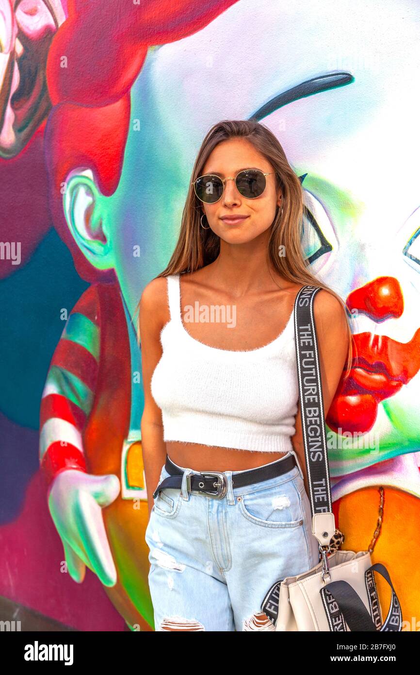 Ein Mittelbild einer jungen Frau, die Sonnenbrille trägt und neben einem dekorativen Graffiti steht, Wynwood Walls, miami, Florida, USA. Stockfoto