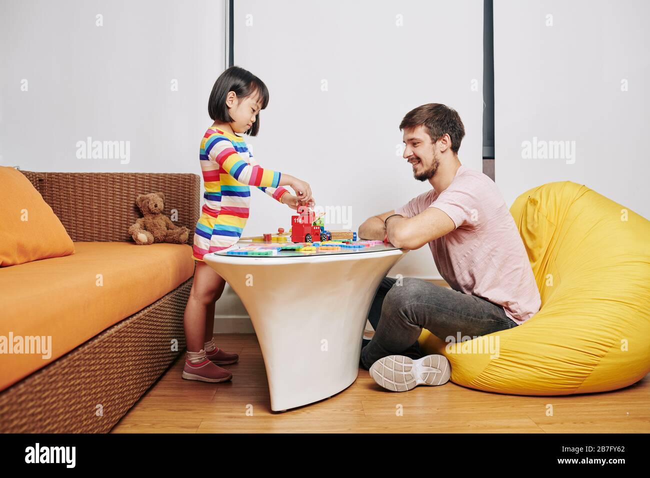 Lächelnder junger Mann, der mit kleiner Tochter spielt, Puzzle macht und Turm baut Stockfoto