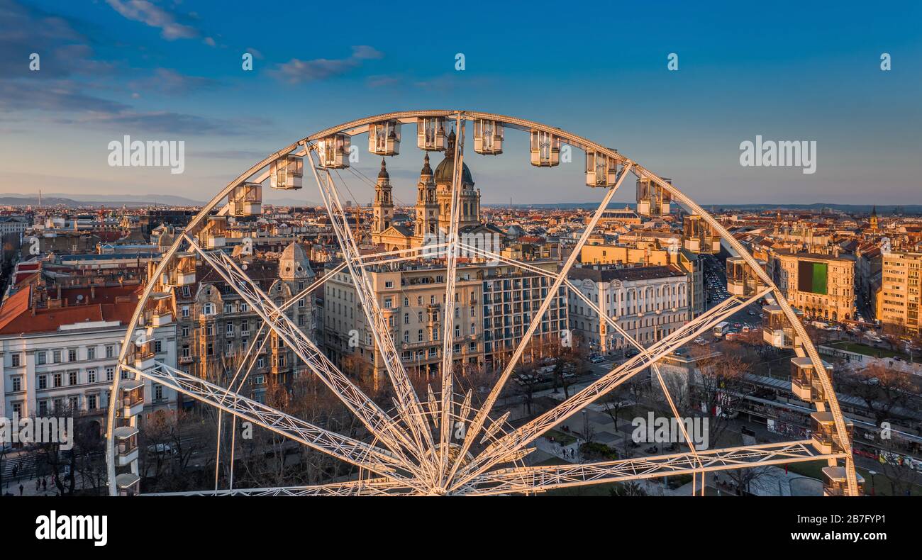 Budapest, Ungarn - Panoramaaussicht auf das Riesenrad am Elisabeth-Platz (Erzsebet ter) bei Sonnenuntergang mit der Stephanusbasilika und dem blauen Himmel bei Stockfoto