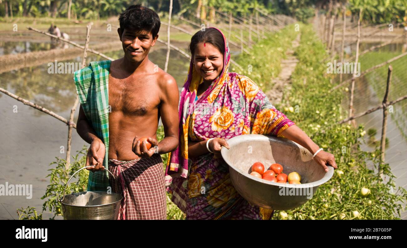 Ein bangladeschisches Paar steht mit einem Lächeln auf dem Gesicht auf einem Teichdeich.im Teich produzieren sie Fische und auf dem Deich produzieren sie verschiedene Gemüsesorten. Stockfoto