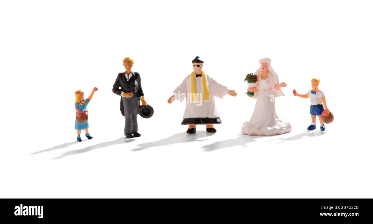 Komplette Hochzeitsgruppe von Miniaturmenschen mit Priester, der zwischen der Brautpaar und einem jungen Blumenmädchen und Seitenjungen über Weiß steht Stockfoto