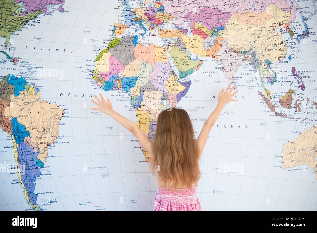 Weltweites Konzept des Reise-Kleinmädchens im Sommerkleid mit Händen nach oben in der Nähe der Weltkarte Stockfoto
