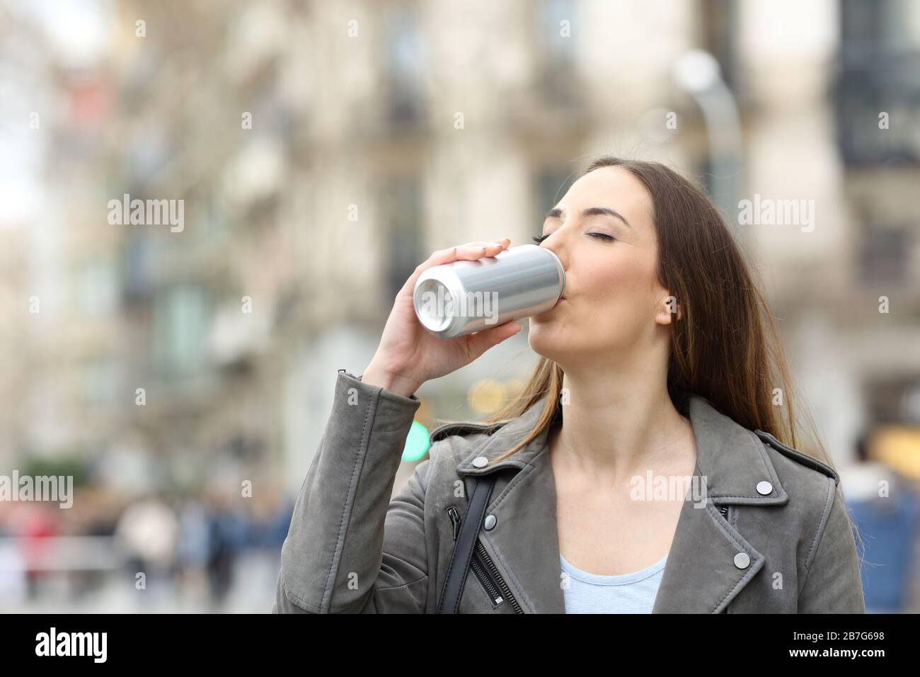 Frau, die eine kalte Erfrischung aus einer leeren Aluminiumkasse auf der Straße trinkt Stockfoto