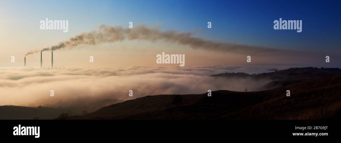 Panoramasicht auf einen Morgenhorizont mit weißen Wolken und drei Röhren, die dunklen Smog in die Atmosphäre ausbringen, Konzept der vom Menschen verursachten Katastrophe, Umweltverschmutzung, Ökologie und Energieerzeugung. Stockfoto