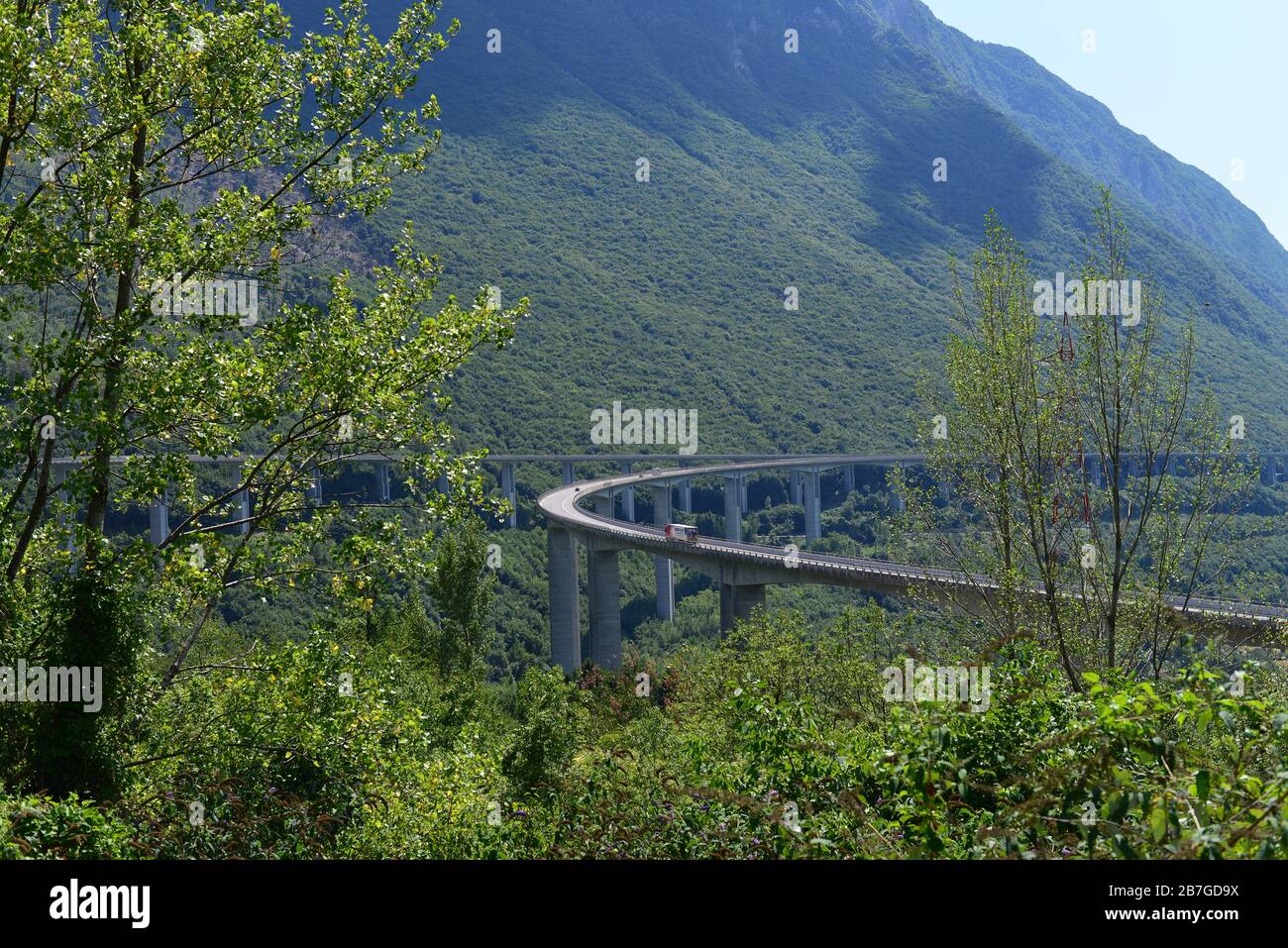 Ein Lieferwagen, der eine erhöhte Autobahn in Norditalien fährt. Die Autobahn ist von Bergen und Vegetation umgeben. Stockfoto