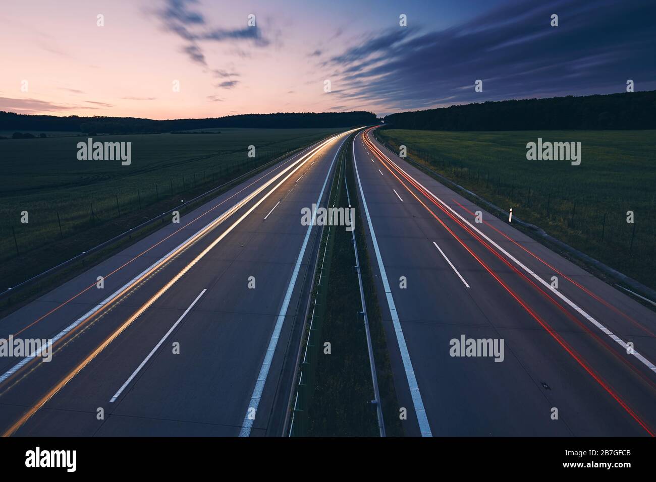 Leichte Wege von Autos. Verkehr auf der Autobahn mitten auf den Feldern bei strahlender Morgendämmerung. Stockfoto