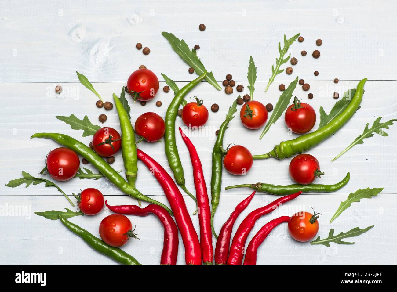 Kirschtomaten in der Nähe von Paprika als Dekoration. Tomaten halbiert mit heißem, würzigen Pfeffer auf grauem Holzhintergrund. Vegetarisches Kunstkonzept. Lebensmittel für die Dekoration mit Gewürzen und Gemüse Stockfoto