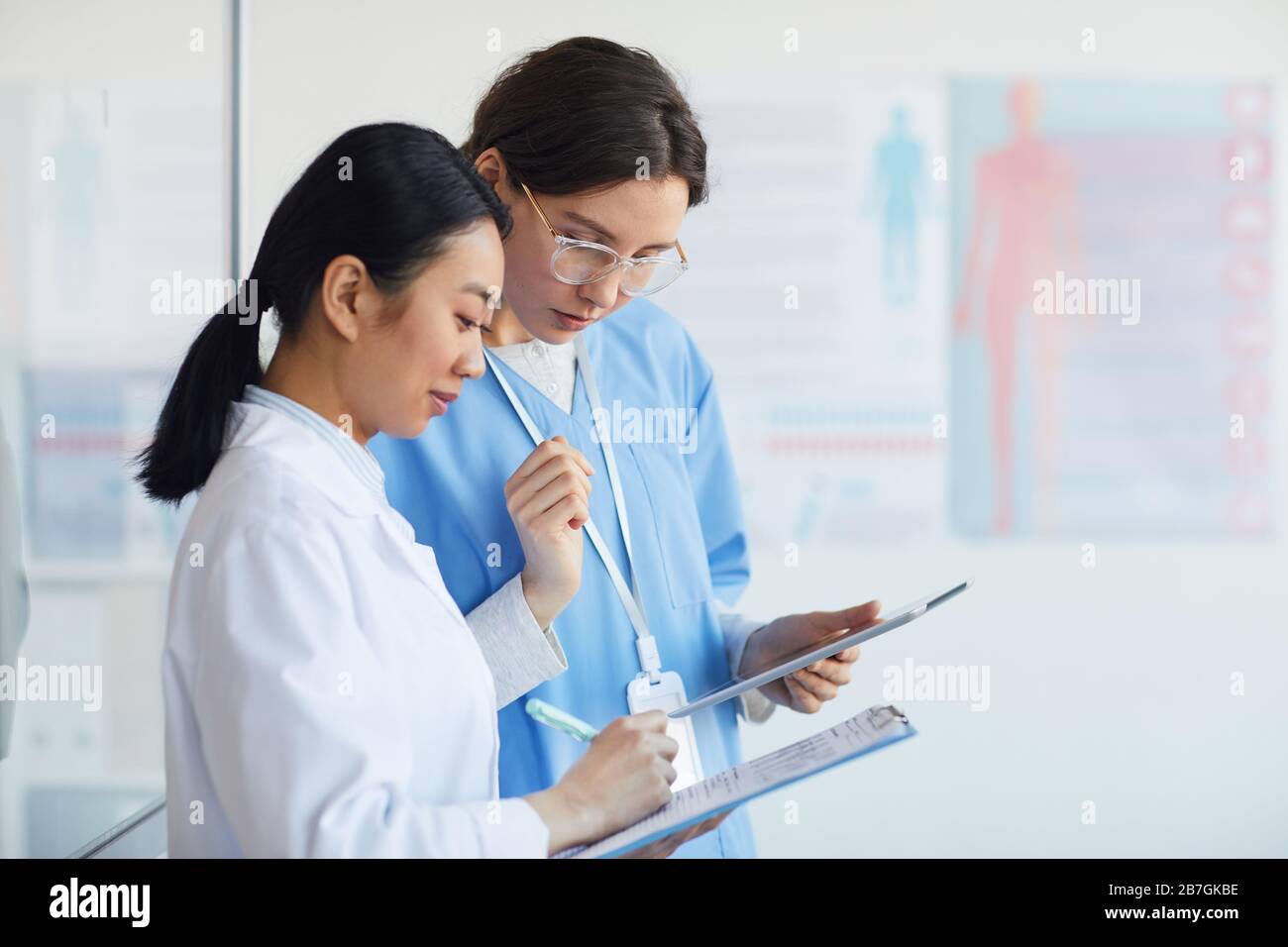 Seitenansicht Porträt von zwei medizinischen Ärzten, die in der Zwischenablage schreiben, während sie im Inneren des medizinischen Büros stehen, Kopierraum Stockfoto