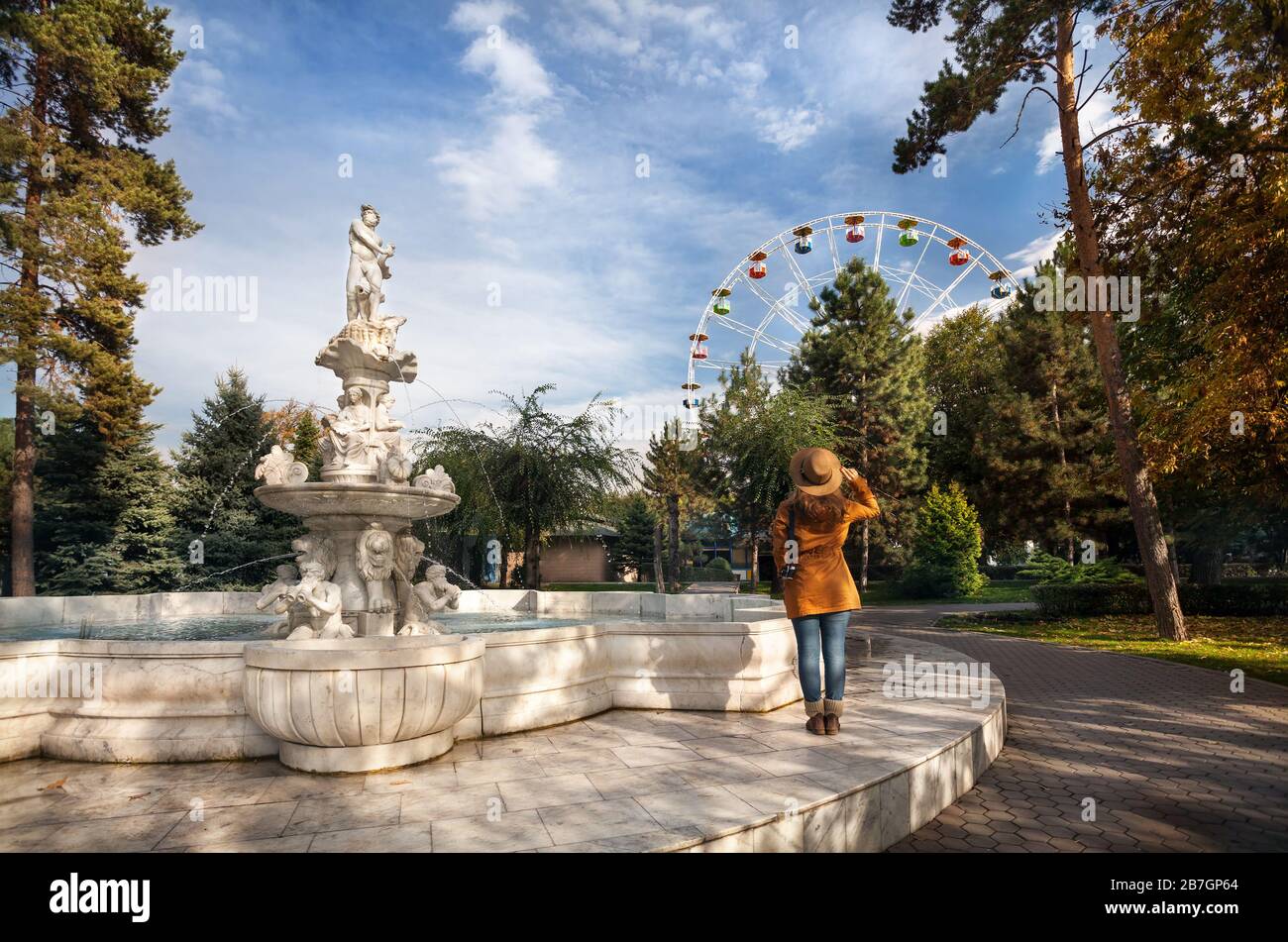 Frau mit Hut in der Nähe von Brunnen mit Statuen betrachten Riesenrad im Herbst park Stockfoto