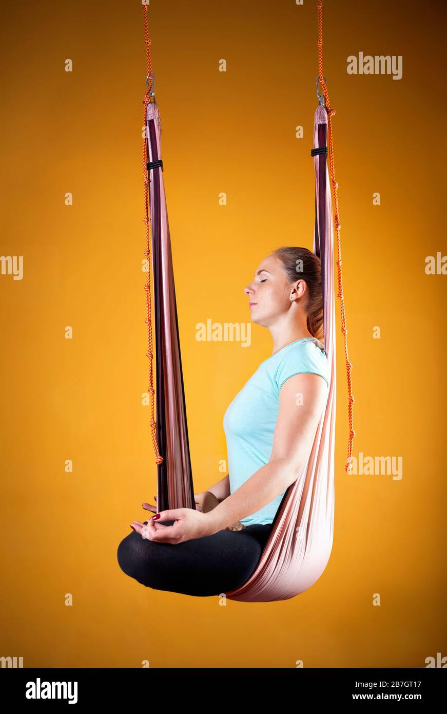 Junge Frau tut Antigravity Yoga meditativen Position auf gelbem Hintergrund Stockfoto
