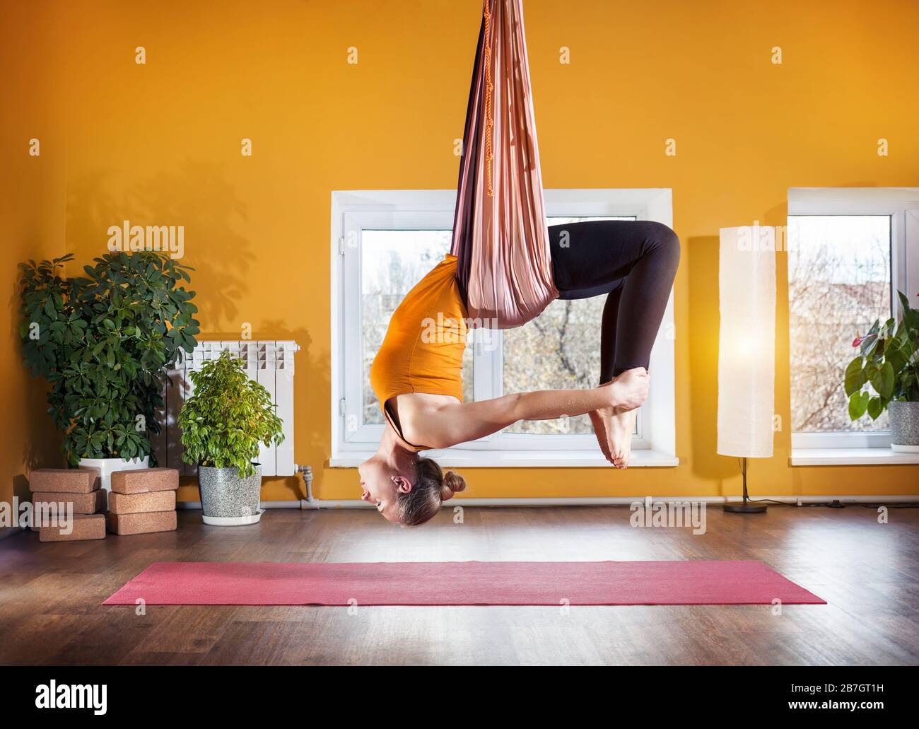 Junge Frau, die nach hinten biegen Position im Studio mit gelben Wänden Antigravity Yoga machen Stockfoto