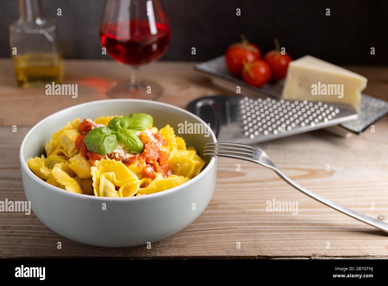 Hausgemachtes Dinner Tortellini mit Tomatensauce arrabbiata und Käse mit einem Glas Wein auf der Seite. Stockfoto