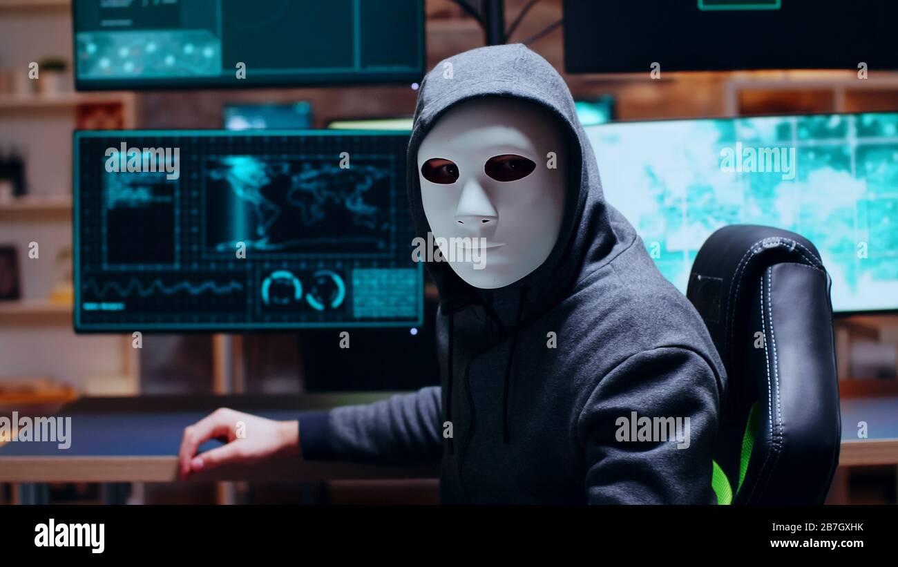 Wollte Cyber-Kriminelle, die eine weiße Maske tragen, während sie die Kamera betrachten. Stockfoto