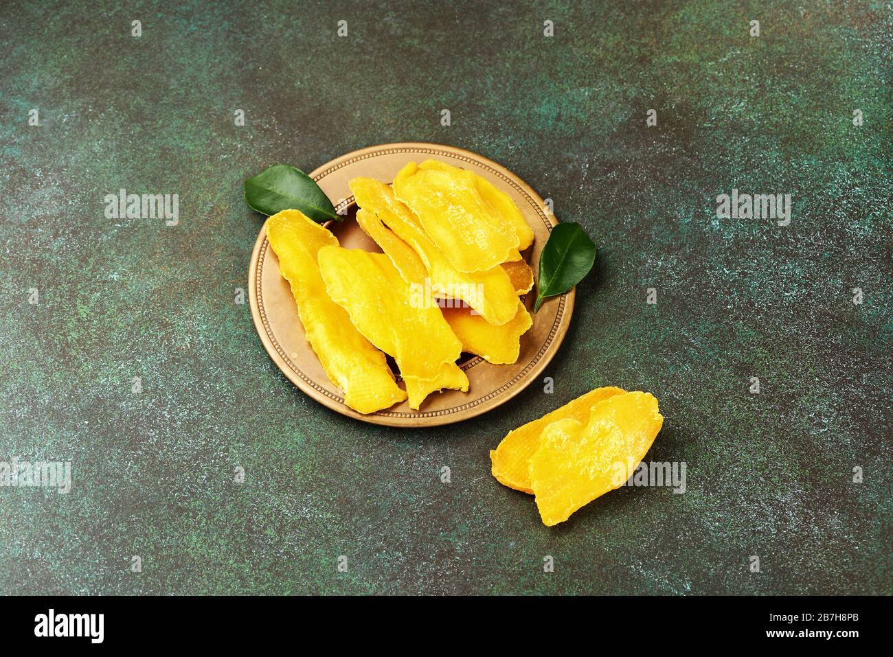 Getrocknete Mango-Früchte mit frischen Blättern auf grünem Grund. Mango in gelber Scheiben. Stockfoto