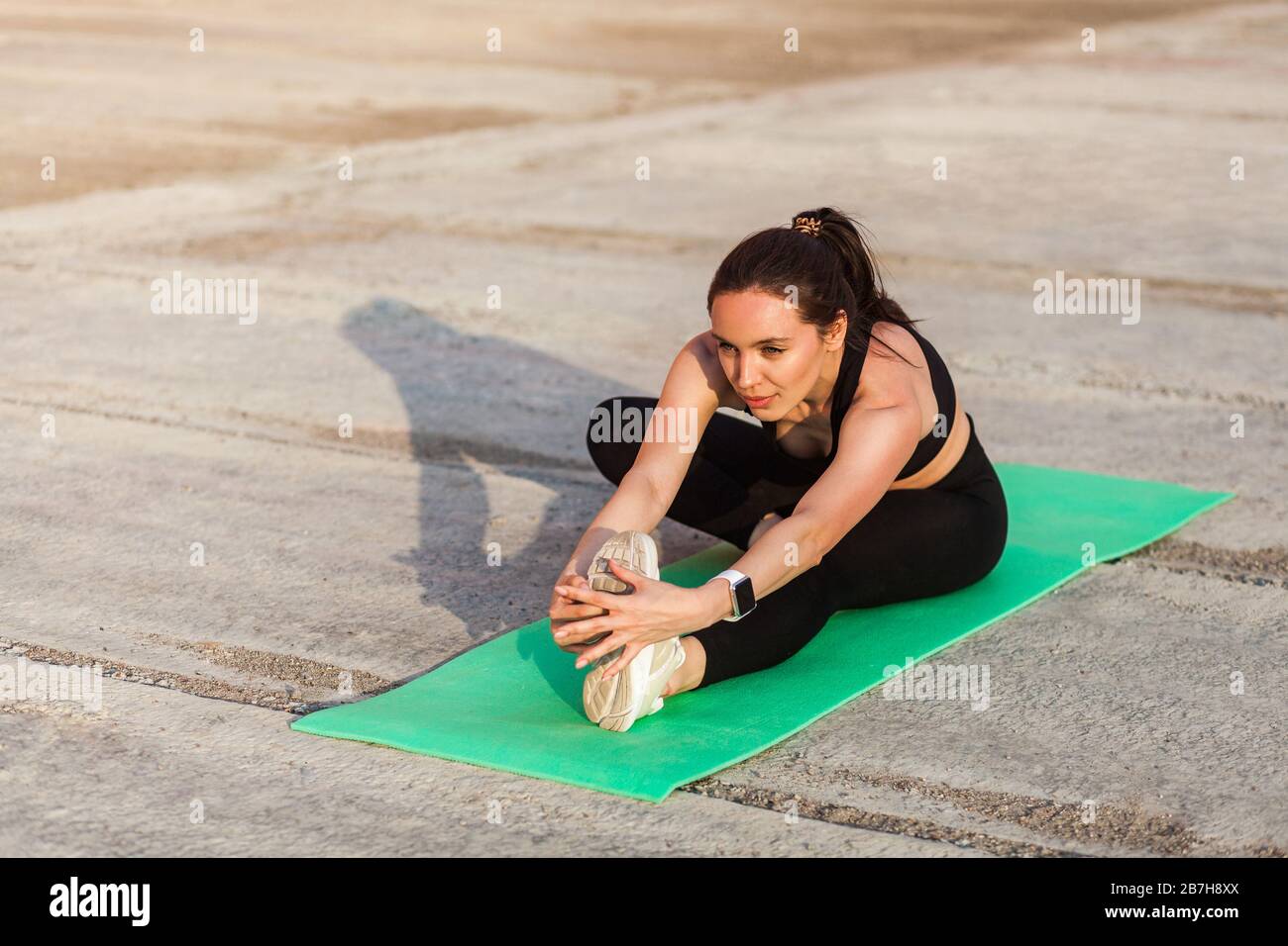 Positive sportliche Passform Frau in enger Sportswear, schwarzer Hose und Oberteil, praktizierendes Yoga, Kopf-Knie-Pose, berührende Zehen, ausdehnendes Bein und Rücken Stockfoto