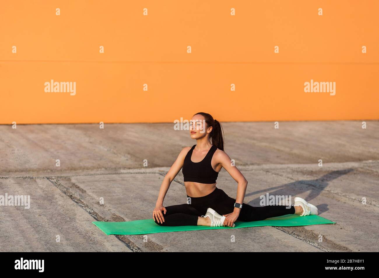 Motivierte, sportlich positive Frau in enger Sportswear, schwarzer Hose und Oberteil, praktizierender Yoga, durchführen einer einbeinigen Königstaubenpose und meditierend, Flexibi Stockfoto