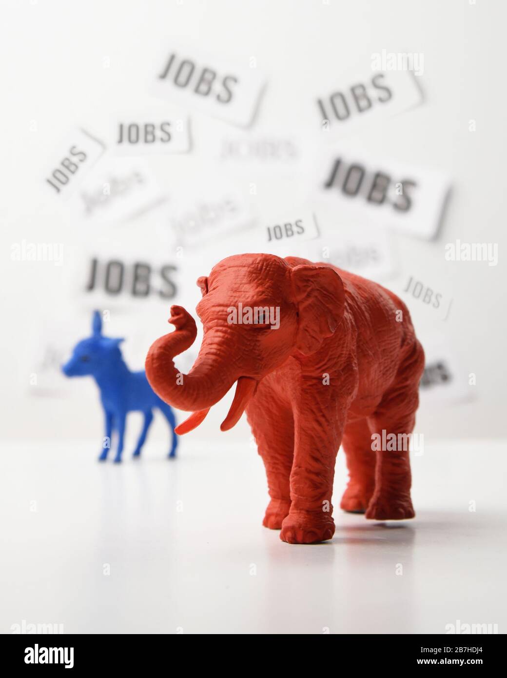 Ein blauer Esel und ein roter Elefant stehen vor einer weißen Wand, die einen Arbeitstext im Hintergrund für eine politische Frage der Beschäftigungsquote 2020 und der eg hat Stockfoto