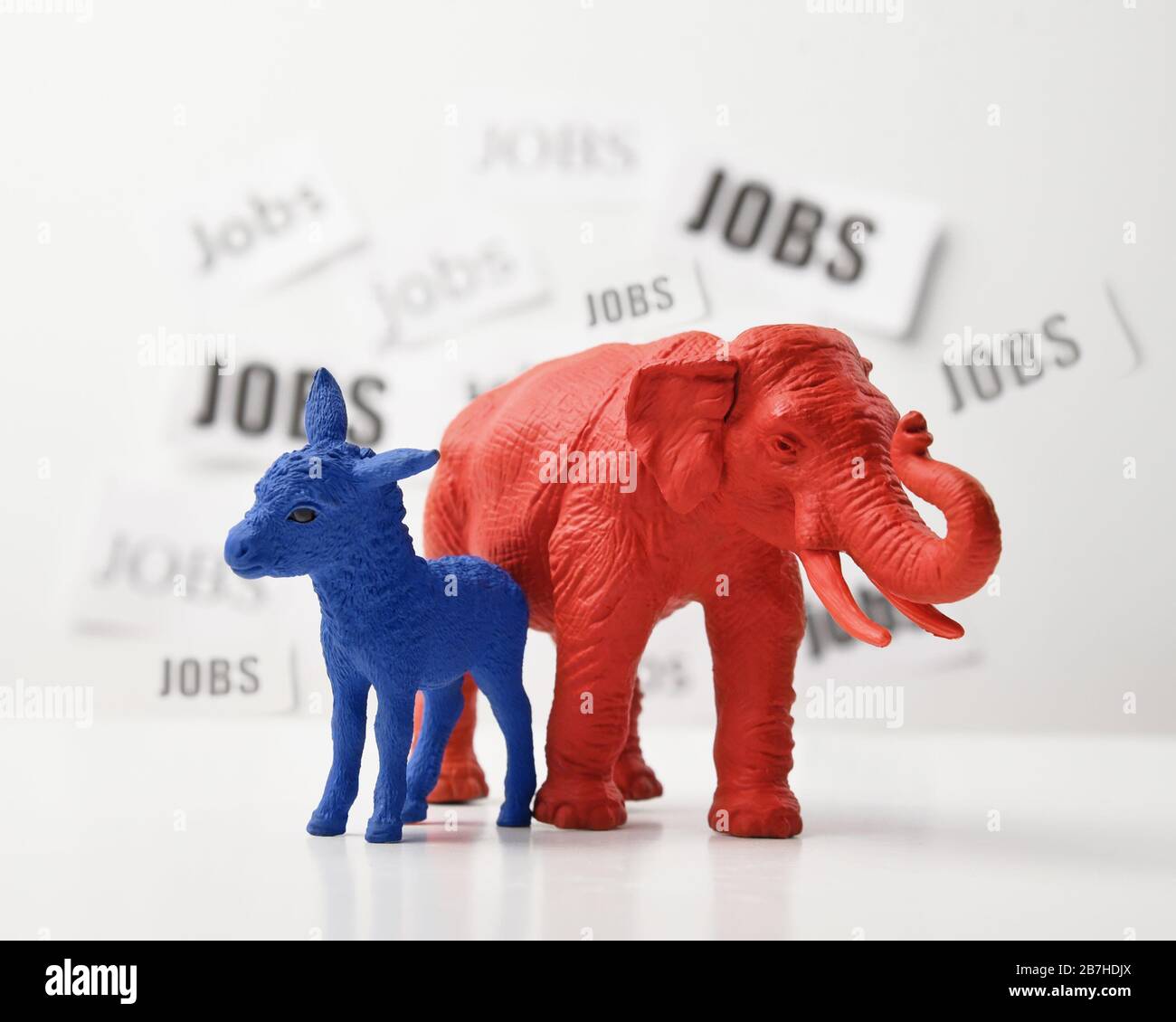 Ein blauer Esel und ein roter Elefant stehen vor einer weißen Wand, die einen Arbeitstext im Hintergrund für eine politische Frage der Beschäftigungsquote von 2020 hat. Stockfoto