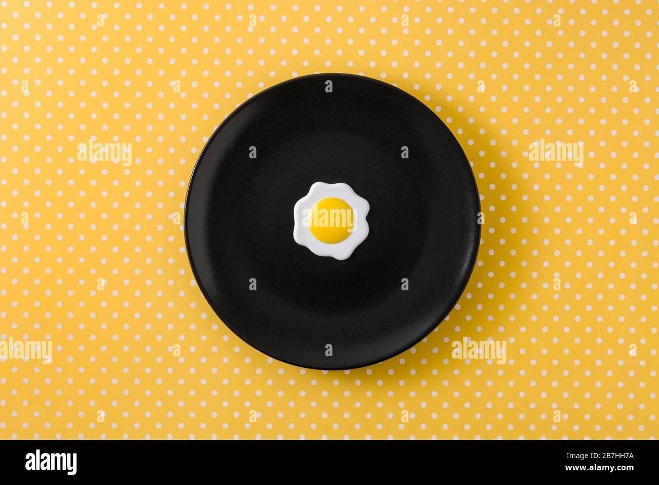 Minimalistisches frittiertes Ei auf schwarzem Teller und gelbem Hintergrund Stockfoto
