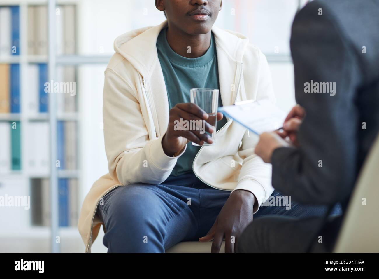 Zugeschnittenes Porträt des jungen afroamerikanischen Mannes, der während der Therapiesitzung Glas Wasser hält, Kopierraum Stockfoto