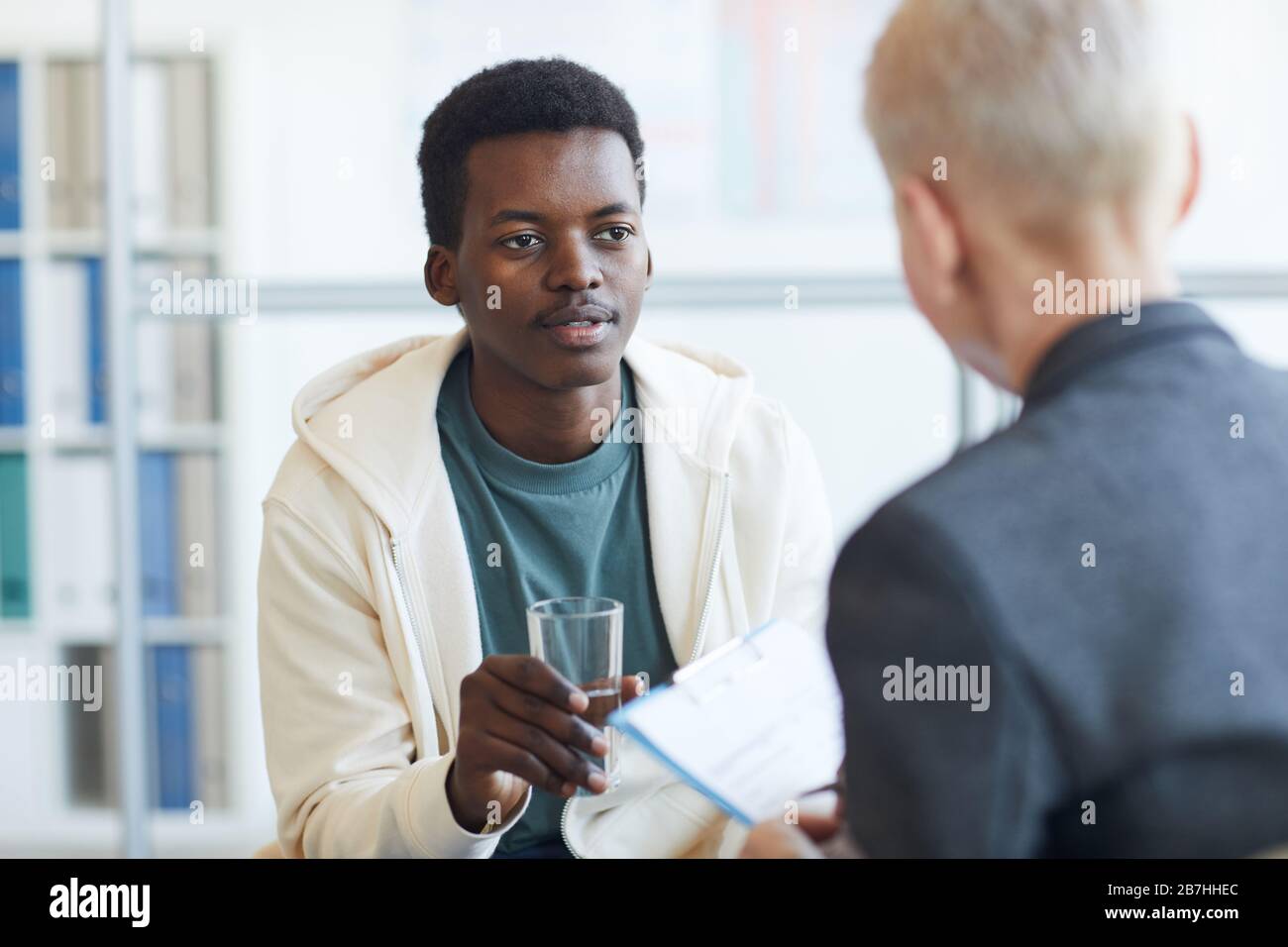 Portrait des jungen afroamerikanischen Mannes, der während der Therapiesitzung Glas Wasser hält, Copy-Space Stockfoto