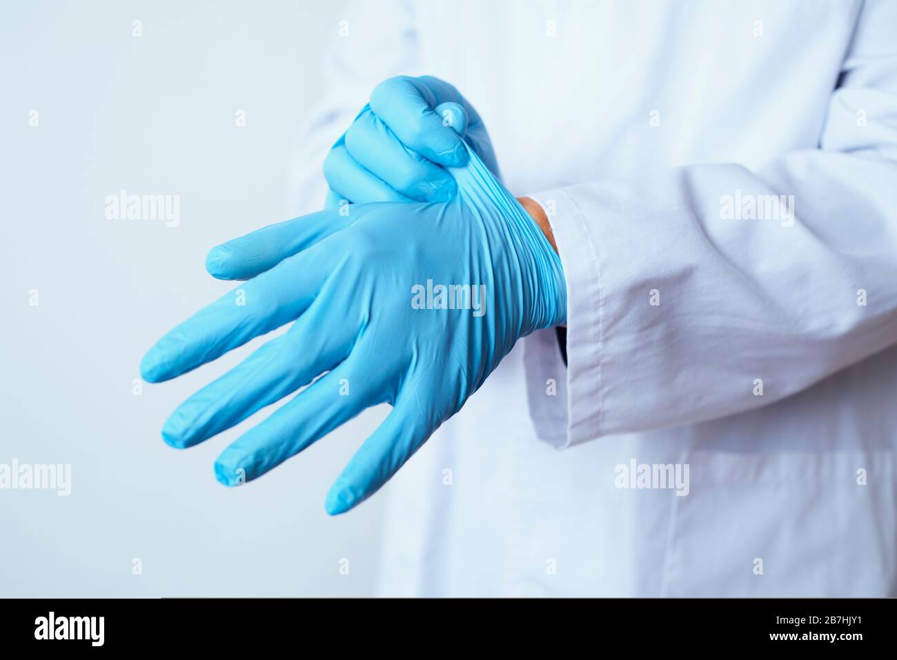 Closeupo eines kaukasischen Arztes, der einen weißen Mantel trägt und ein Paar blauer chirurgischer Handschuhe anlegt Stockfoto