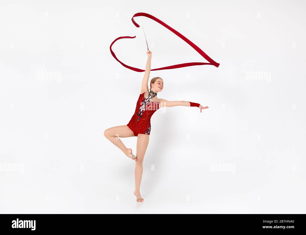 Schöne Turnerin in Rotleotard, die Übungen mit Band auf weißem Hintergrund macht Stockfoto