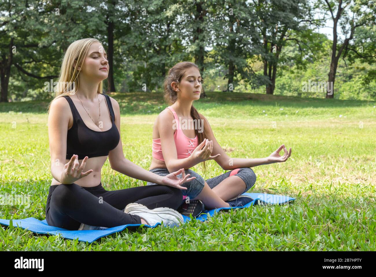 Glückliche gesunde zwei Frauen Teenager trainieren und praktizieren Padmasana oder lotus Yoga Pose am Wochenende im Park. Gesund, Sport und Lifestyl Stockfoto