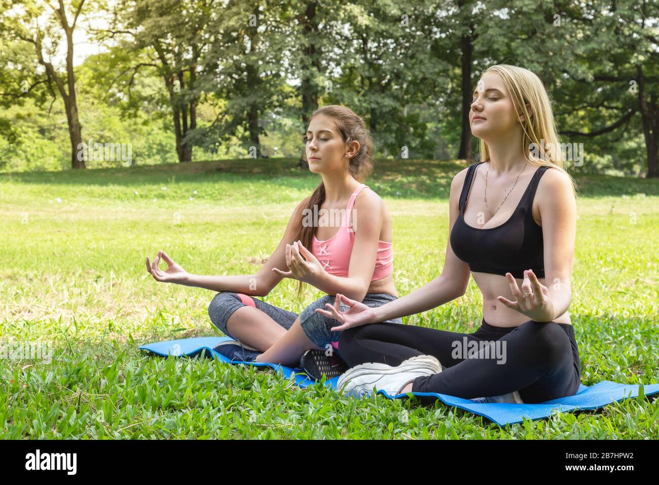 Glückliche gesunde zwei Frauen Teenager trainieren und praktizieren Padmasana oder lotus Yoga Pose am Wochenende im Park. Gesund, Sport und Lifestyl Stockfoto