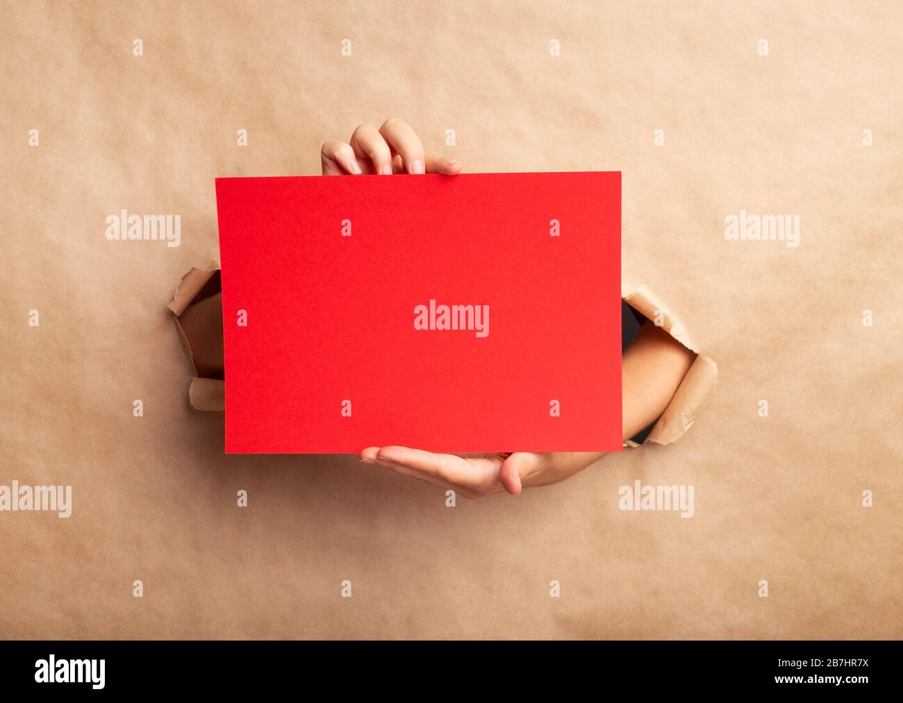 Frau hält rotes Blatt mit Platz für Design durch Loch in geripptem braunem Papier, Nahaufnahme Stockfoto
