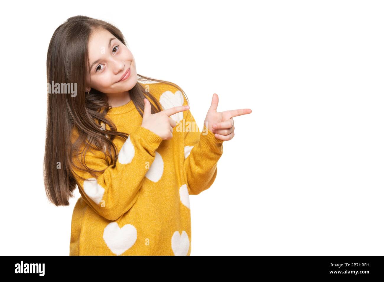 Schönes junges Mädchen im senfgelben Pullover mit Blick auf die Kamera, lächelnd und zur Seite zeigend. Studio mit Taille oben, aufgenommen auf weißem Hintergrund. Stockfoto