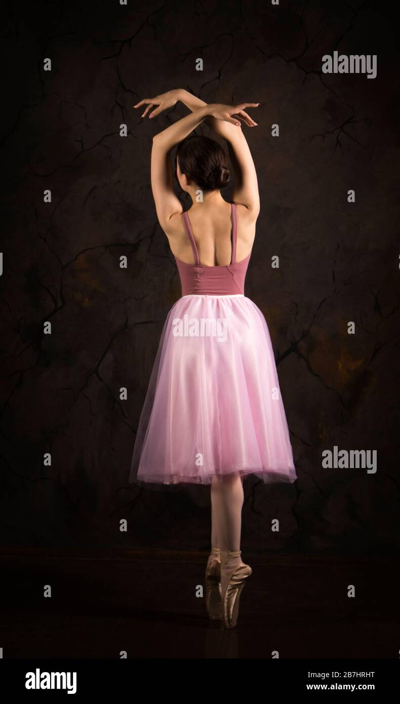 Eine schlanke Frau in einem rosa Rock und beige Top tanzen Ballett. Studio-Aufnahmen vor dunklem Hintergrund, isolierte Bilder. Stockfoto