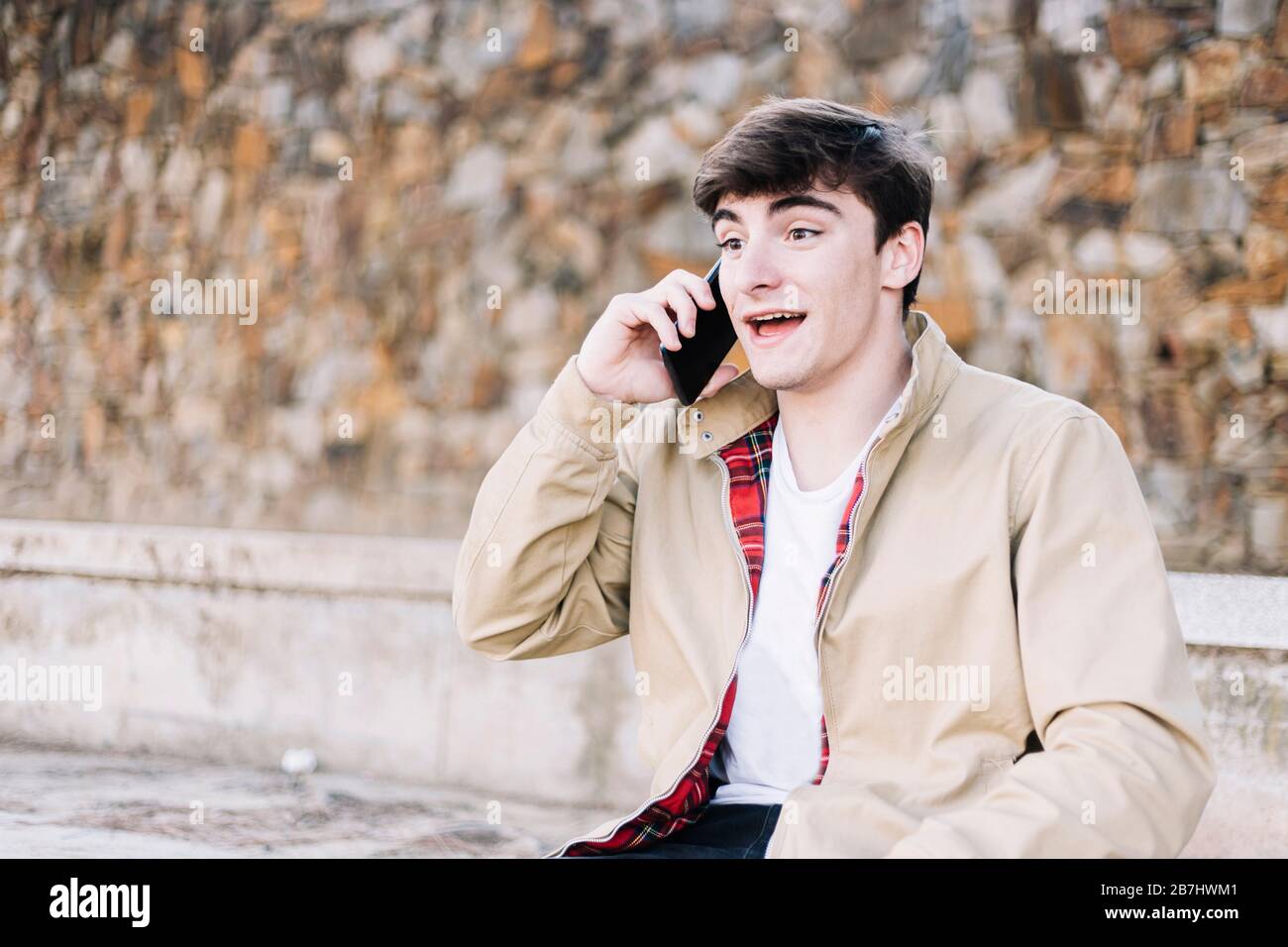 Junger Mann, der im Freien mit dem Handy sitzt Stockfoto