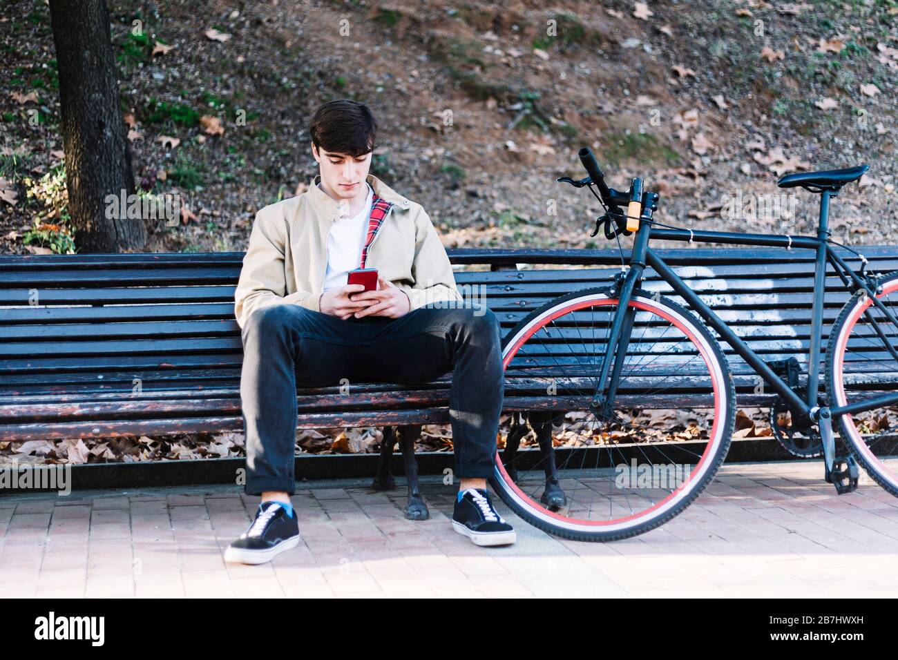 Junger Mann, der im Freien mit dem Handy sitzt Stockfoto