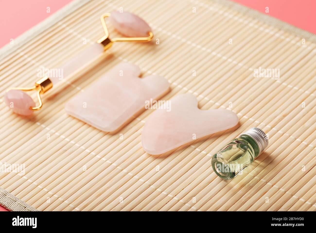 Gua sha-Massage aus natürlichem Rosen-Quarz-Roller, Jadestein und Öl, auf Bambushintergrund für Gesichts- und Körperpflege. Stockfoto