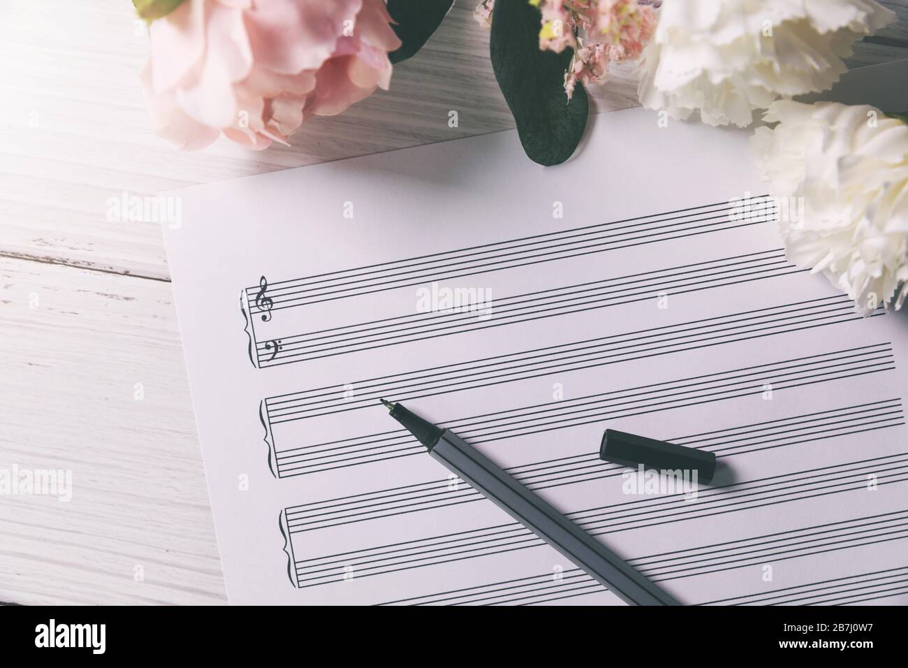 Leeres Notenblatt mit Blumen und Stift auf weißem Holztisch Stockfoto