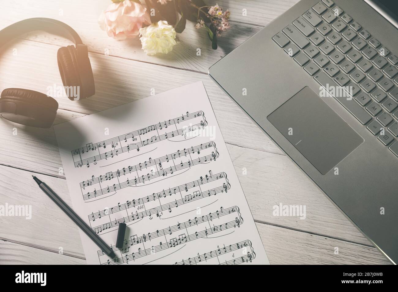 Musik und Bildung komponieren - Papierblatt mit Musiknotizen, Laptop und Kopfhörer auf dem Schreibtisch des Künstlers Stockfoto