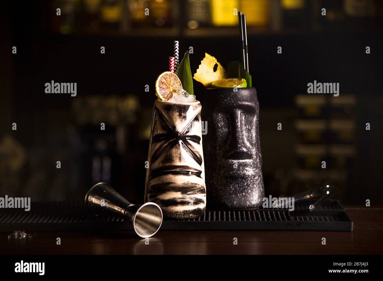 Tiki Trinken Cocktails. Zwei Cocktails in verschiedenen Gläsern vor dem Hintergrund einer Bar mit getrockneten Früchten und tropischen Blättern. Stockfoto