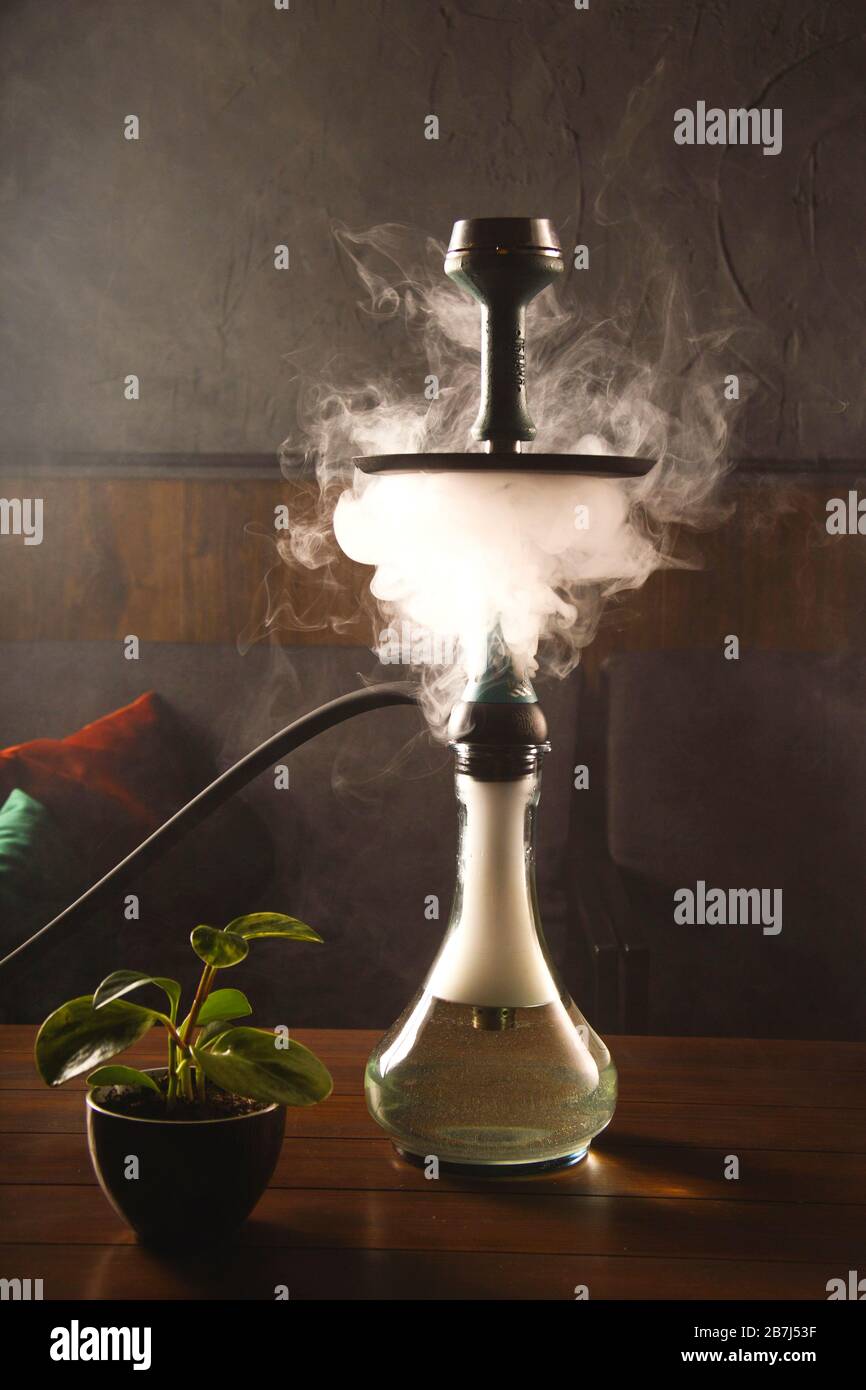 Rauch aus einer Kapuze in einer Bar auf einem Tisch auf dunklem Hintergrund. Rauchen für Entspannung. Stockfoto
