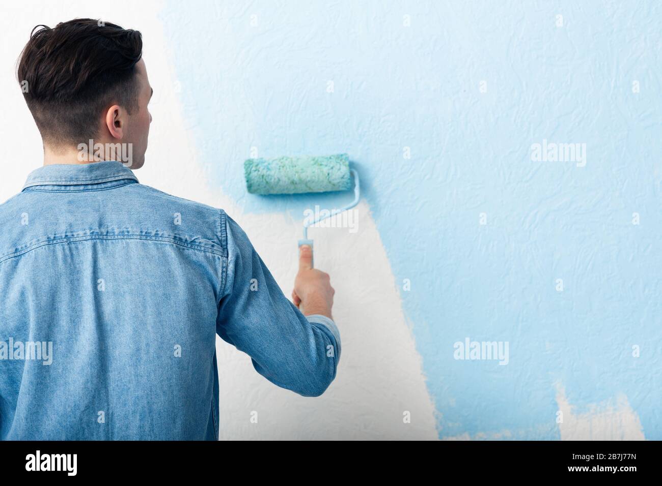 Mann malt Innenwand mit Lackierwalze Stockfoto