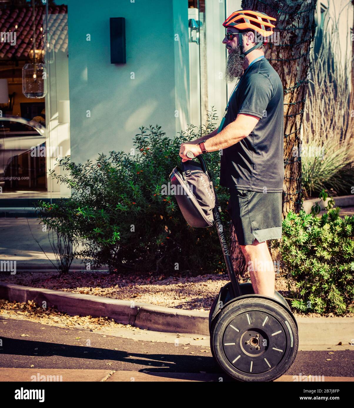 Ein Mann mit einem Hüftbart und einem orangefarbenen Helm navigiert seinen Segway-Personentransporter in der Altstadt von Scottsdale, AZ, Stockfoto