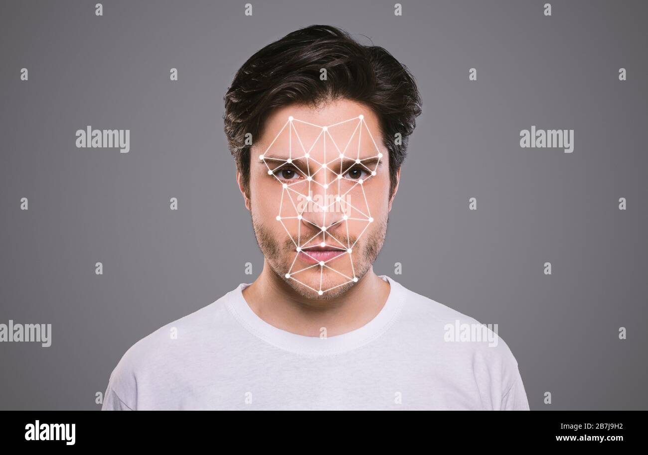 Biometrische Identifikation. Junger Mann, der vor grauem Hintergrund mit polygonalem Mesh auf seinem Gesicht auf die Kamera blickt Stockfoto