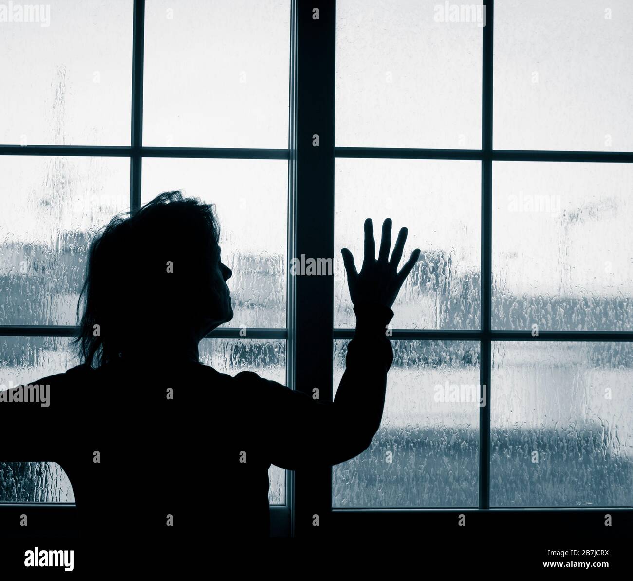 Frau, die am regnerischen Tag aus dem Fenster schaut. Bild des Verständigen; weibliche Depression, häuslicher Missbrauch, Selbstisolierung, Quarantäne, Coronavirus, Stockfoto