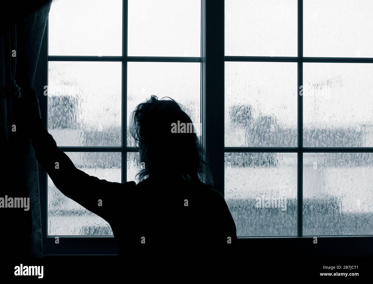 Frau, die am regnerischen Tag aus dem Fenster schaut. Bild des Verständigen; weibliche Depression, häuslicher Missbrauch, Selbstisolierung, Quarantäne, Coronavirus, Stockfoto