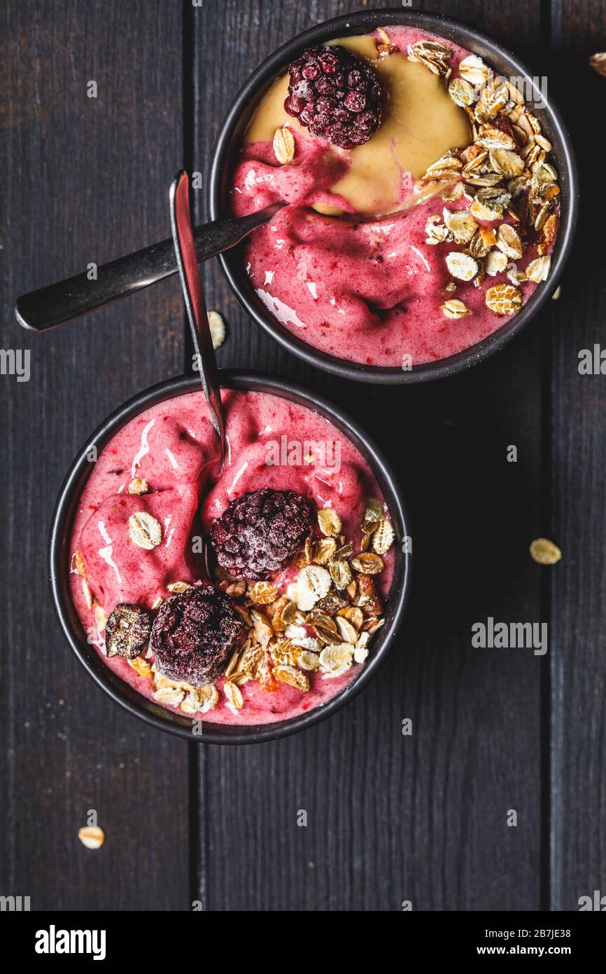 Vegane Beere Smoothie Schüssel mit Tahini und Müsli, dunkler Hintergrund. Hausgemachtes Beereneis mit Erdnussbutter und Granola. Stockfoto