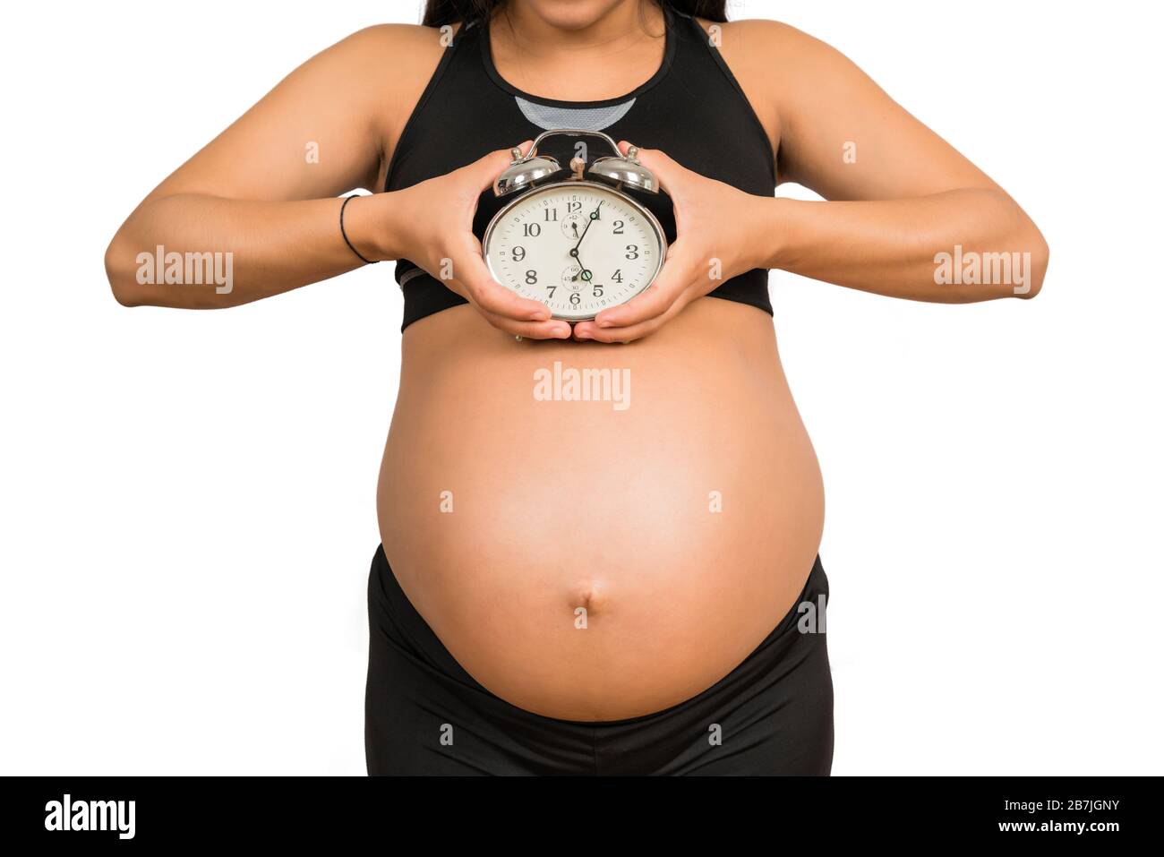 Nahaufnahme der schwangeren Frau, die einen Wecker hält und ein Baby erwartet. Schwangerschaft, neues Konzept für Mutter und Mutterschaft. Stockfoto