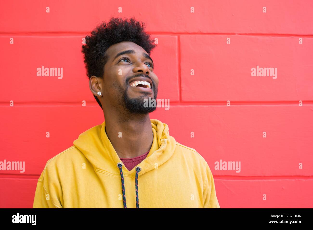 Porträt eines jungen afro-amerikanischen Mannes, der selbstbewusst aussieht und gegen die rote Wand posiert. Stockfoto